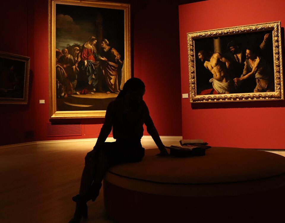 Silhouetted visitor in art gallery with dramatic lighting on paintings